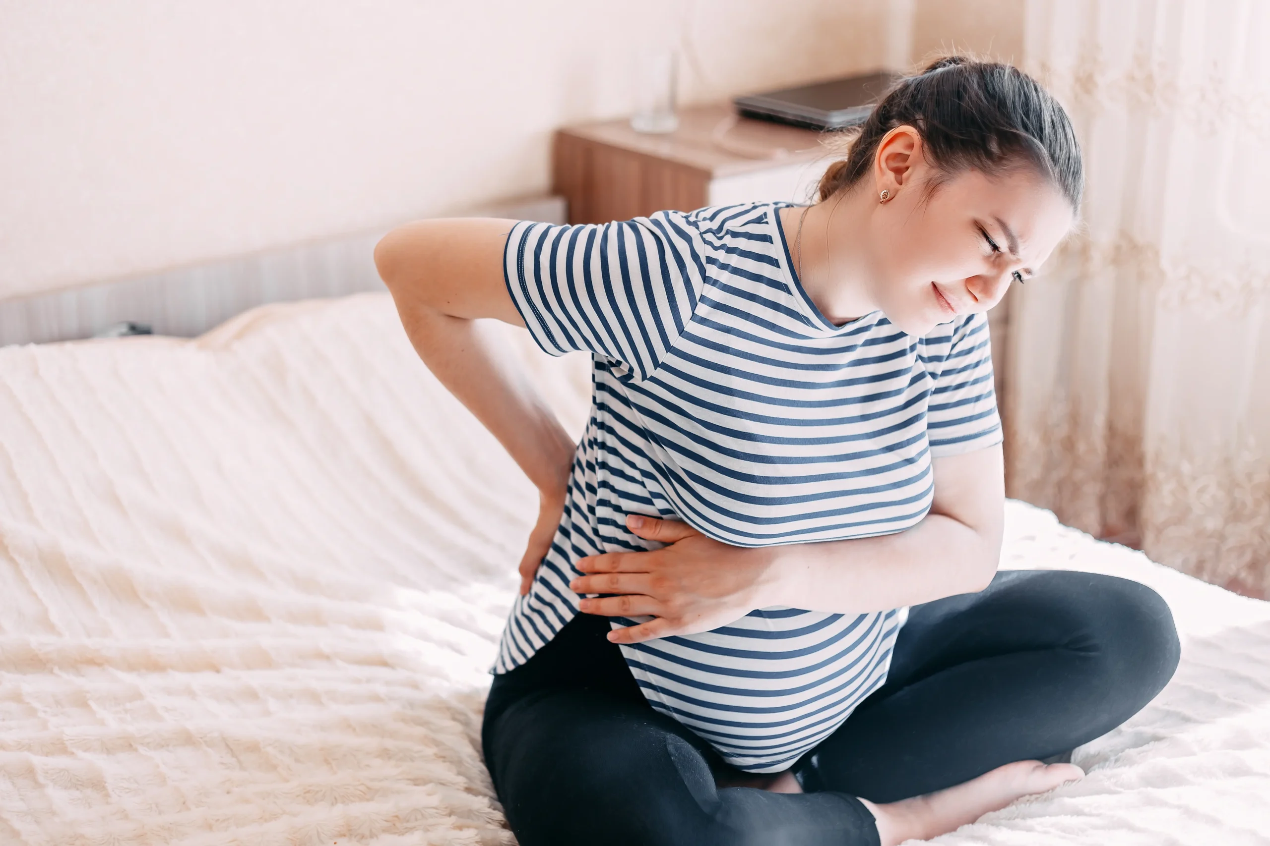 Douleurs aux côtes pendant la grossesse : comment les soulager ? 2 adult woman sitting on bed with stomach pain 2026 03 19 02 58 17 utc scaled